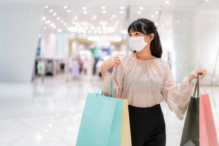 Asian woman wearing mask over her face while walking at shopping mall with shopping bag for healthcare and prevention from coronavirus, Covid19 influenza in crowded place.の写真素材