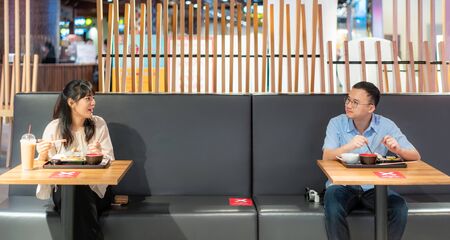 Asian man and woman eating food on table by one person one table for social Distancing 6 feets concept protection of Coronavirus Covid-19 at food court in Bangkok, Thailand.の写真素材