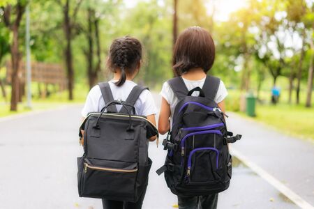 Two pupils of primary school walking go to shool. Two girl with bags behind the back. Warm day of fall. Back to school. Little first graders.
の写真素材