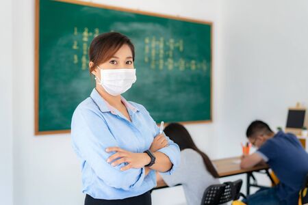 Asian woman teacher wearing masks to prevent the outbreak of Covid 19 in classroom with student while back to school reopen their school, New normal for education concept.の写真素材