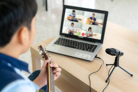 Asian boy playing acoustic guitar virtual happy hour meeting for play music online together with friend in video conference with laptop for a online meeting in video call for social distancing.の写真素材