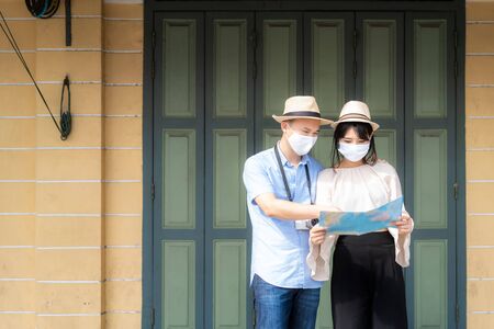 Asian couple happy tourists to travel wearing mask to protect from Covid-19 on they holidays and holding travel map in old town in Bangkok, Thailandの写真素材