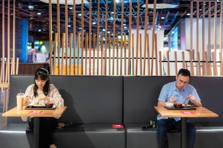 Asian man and woman eating food on table by one person one table in food court for social Distancing 6 feets concept protection of Coronavirus Covid-19 at food court in Bangkok, Thailand.の写真素材