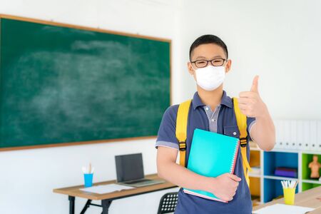 Asian primary students boy thumb up and  wearing masks to prevent the outbreak of Covid 19 in classroom while back to school reopen their school, New normal for education concept.の写真素材