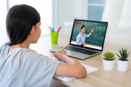 Asian girl student video conference e-learning with teacher on computer in living room at home. Homeschooling and distance learning ,online ,education and internet protect from COVID-19 viruses.の写真素材