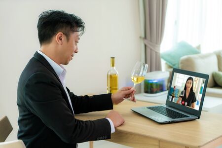 Asian man virtual happy hour meeting party and drinking white grape wine online together with his friend in video conference with digital tablet for a online meeting in video call for social distancing.の写真素材