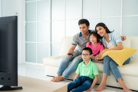 Asian happy family with father, mother, son and daughter sitting in sofa and watching television at home concept of family values, vacation day, holiday, happiness or lifestyle.の写真素材