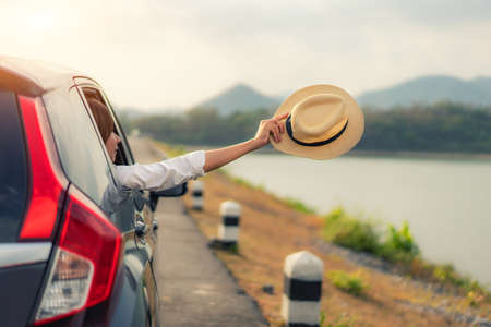 Woman at spree time relaxing and enjoying road trip. Young Asian happines female inside compact black car with raise her hat out to the car window with mountain and lake view at sunny day in Thailand.
の写真素材