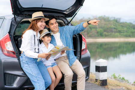 Portrait of Asian family sitting in car with father pointing to view and mother with daughter looking beautiful landscape and holding maps while vacation together in holiday. Happy family time.の写真素材