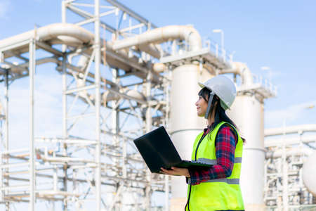 Asian woman petrochemical engineer working at night with laptop Inside oil and gas refinery plant industry factory at night for inspector safety quality control.の写真素材