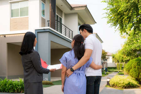 Asian woman Real estate broker agent showing a house detail in her file to the young Asian couple lover looking and interest to buy it. Buying a new house.の写真素材