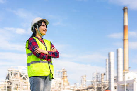 Asian woman engineer arm crossed and smile with confident looking forward to future with oil refinery plant factory in background.の写真素材