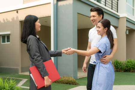 Happy Asian couple looking for their new house and shake hands with real estate broker after a deal. Young couple handshaking real estate agent after signing contract for buy house.の写真素材