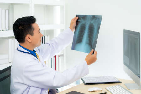 Asian man doctor holding and looking to examining x-ray of the patientâs lungs and brain in a medical clinic at hospital.の写真素材
