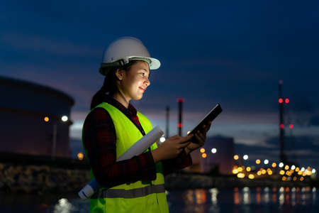 Asian woman petrochemical engineer working at night with digital tablet Inside oil and gas refinery plant industry factory at night for inspector safety quality control.の写真素材