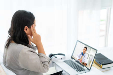Asian woman in white bed speaking with doctor using tele-health technologyの写真素材