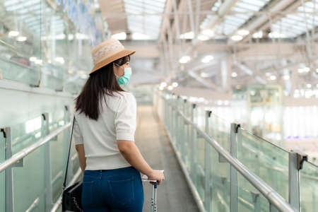 Asian traveler  woman with luggage wearing face mask looking outside terminal in airport standing on escalator go to gate for journey.の写真素材