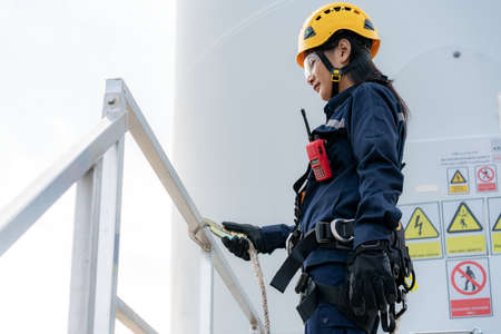 Asian woman Inspection engineer wearing safety harness and safety line working preparing and progress check of a wind turbine with safety in wind farm in Thailand.の写真素材