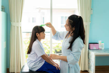 Asian Mother is combing her daughter's hair on the morning before going to school in living room at home. The morning school routine for day in the life getting ready for schoolの写真素材