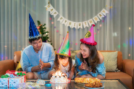 Asian happy family in a birthday party for her daughter while daughter is about to blow out the candles at night in living room at home.の写真素材