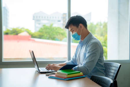 Asian university student boy wearing face protective medical mask for protection from virus disease working with laptop at college. Education, high school, university, learning and people conceptの写真素材