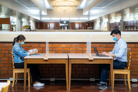 Two Asian university students wearing face mask and sitting in library social distance from other 6...