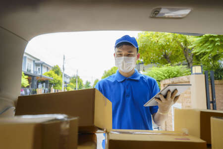 Asian Delivery man services courier working with cardboard boxes on van during the Coronavirus (COVID-19) pandemic, courier wearing medical mask and latex gloves for safety.の写真素材