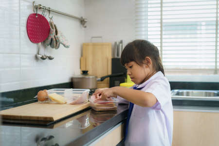 Asian elementary school student girl in uniform making sandwich for lunch box in morning school routine for day in life getting ready for school.の写真素材