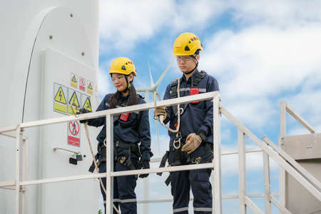Asian man and woman Inspection engineers preparing and progress check of a wind turbine with safety in wind farm in Thailand.の写真素材
