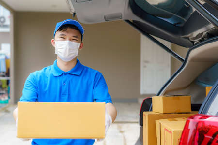 Asian Delivery man services courier working with cardboard boxes on van during the Coronavirus (COVID-19) pandemic, courier wearing medical mask and latex gloves for safety.の写真素材