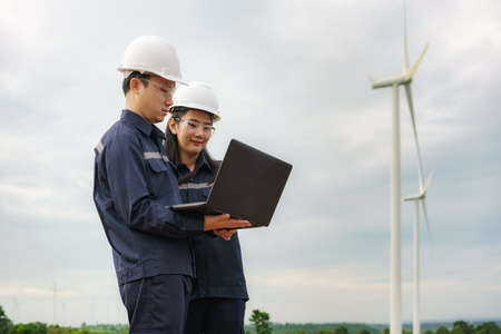 Asian man and woman Inspection engineers preparing and progress check with laptop of a wind turbine with safety in wind farm in Thailand.の写真素材