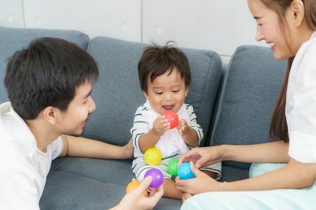 Portrait of Asian cute baby boy playing colorful plastic balls with father and mother on sofa with...