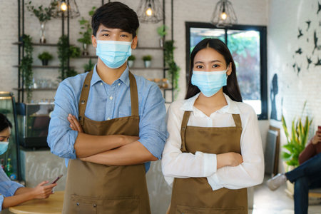 Asian Barista couple in apron and face mask looking at camera ready to give Coffee Service at the modern coffee shopの写真素材