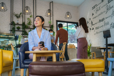 Asian woman sitting in cafe and feeling happy while she drink coffee and another people wears face mask to prevent COVID-19.の写真素材