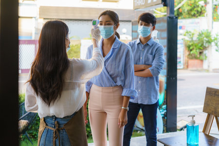 Asian woman cafe employee take temperature Asian woman with face mask before go to restaurant or...