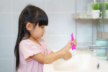 Asian cute child girl or kid Squeeze the toothpaste into toothbrush before brushing her teeth in the bathroom. Dental hygiene Healthcare concept.の写真素材