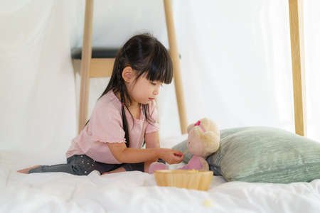 Asian cute little girl play her doll and feeding snack while sitting in a blanket fort in living room at home for perfect hideout away from their other family members and for them to play imaginatively.の写真素材