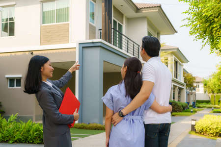 Asian woman Real estate broker agent showing a house detail in her file to the young Asian couple lover looking and interest to buy it. Buying a new house.の写真素材