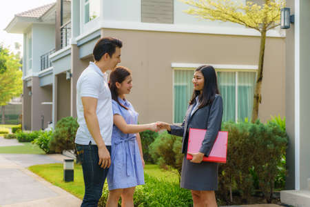 Happy Asian couple looking for their new house and shake hands with real estate broker after a deal. Young couple handshaking real estate agent after signing contract for buy house.の写真素材