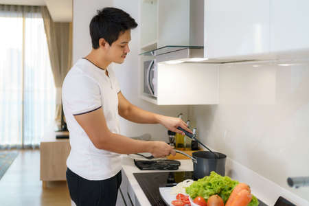 Asian man are using a ladle to thicken vegetable soup in a pot at the home kitchen.の写真素材