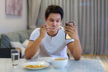 An Asian man sitting at the dinner table and had a video call talking to his girlfriend for social...
