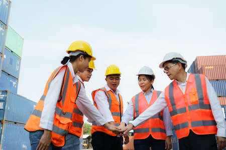 Asian foreman and his team worker standing hands holding together at the container depot terminal for unity and success concept.の写真素材