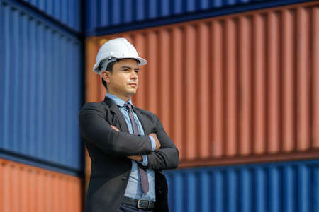 A Caucasian businessman is standing up and arm crossed to look at containers, planning a future, investing in a shipping business with containers in background.の写真素材