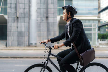 Asian businessman in a suit is riding a bicycle on the city streets for his morning commute to work. Eco Transportation Concept.の写真素材