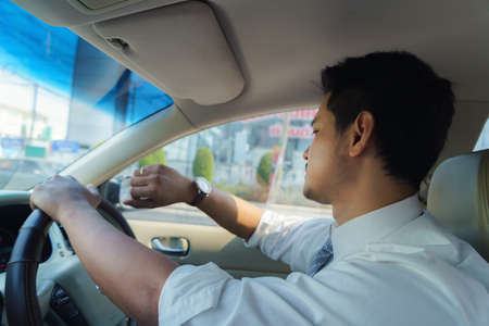 Asian man watches his watch as he drives to work in the morning, late for work. Traffic congestionの写真素材