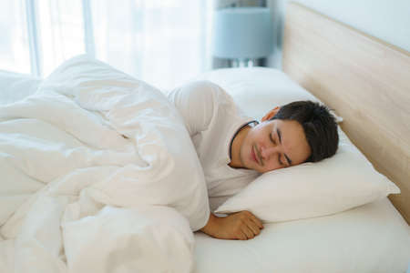 Asian man are sleeping and having good dreams in white blanket in the morning. Rest after work tiring in bedroom at homeの写真素材