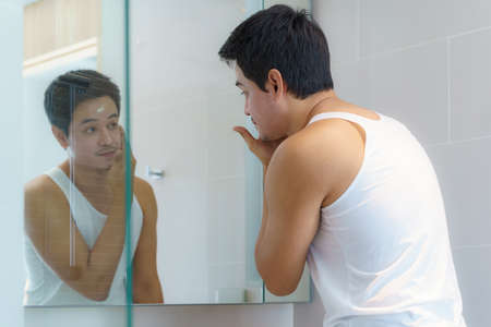 Asian man are applying moisturizer facial cream to his face after bathing and getting ready to work in the bathroom in the house.の写真素材