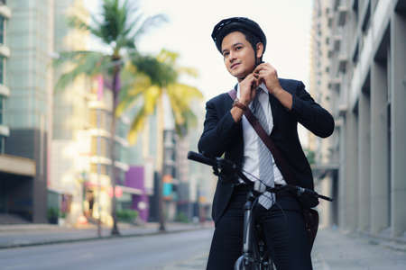 Asian businessman in suits are wearing safety helmets to cycle on city streets for their morning commute to work. Eco transportation.の写真素材