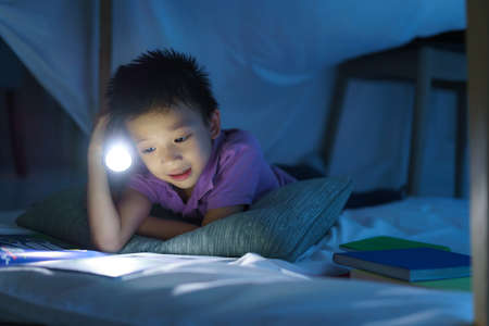Asian preschool boy child to make a camp to play imaginatively and reading book by flashlight  in living room at home.の写真素材