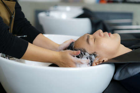 Hairdresser is applying shampoo and massaging hair of a customer. man having his hair washed in a hairdressing salon.の写真素材
